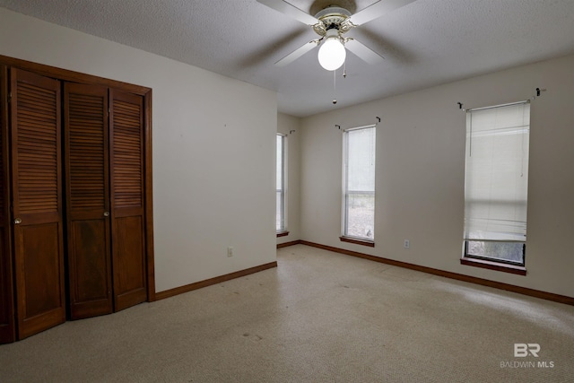 unfurnished bedroom featuring ceiling fan, a textured ceiling, light carpet, and a closet