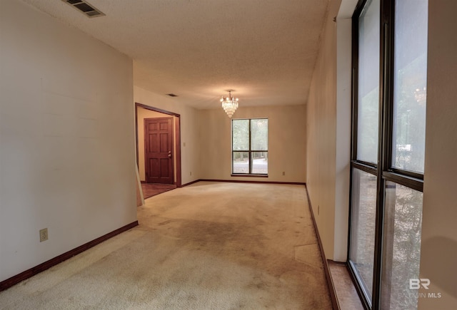 carpeted empty room with a textured ceiling and an inviting chandelier