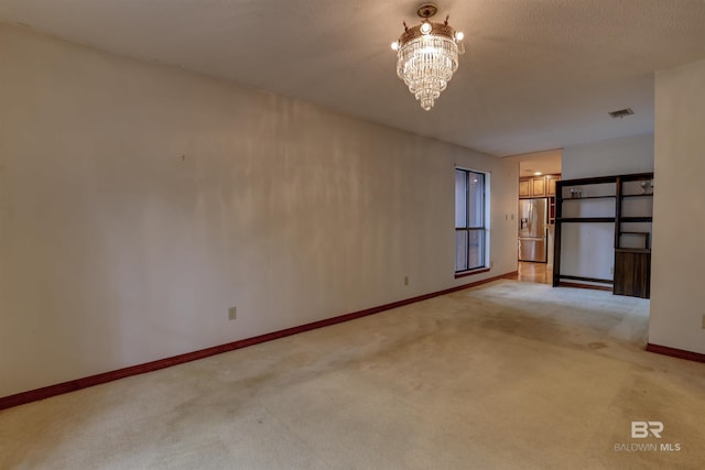 spare room with light colored carpet, a textured ceiling, and an inviting chandelier