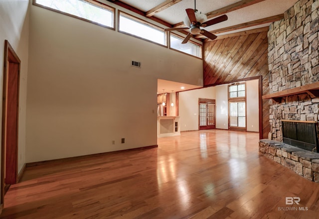 unfurnished living room with a wealth of natural light, a fireplace, high vaulted ceiling, and beamed ceiling