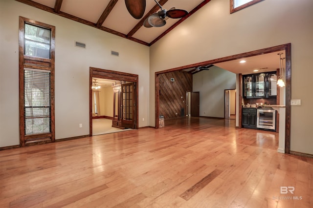 unfurnished living room with beverage cooler, indoor bar, high vaulted ceiling, and light hardwood / wood-style flooring