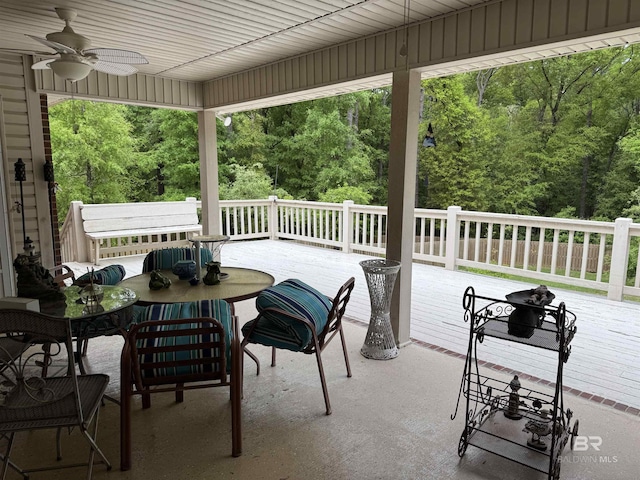 view of patio / terrace featuring a view of trees, outdoor dining area, a wooden deck, and a ceiling fan