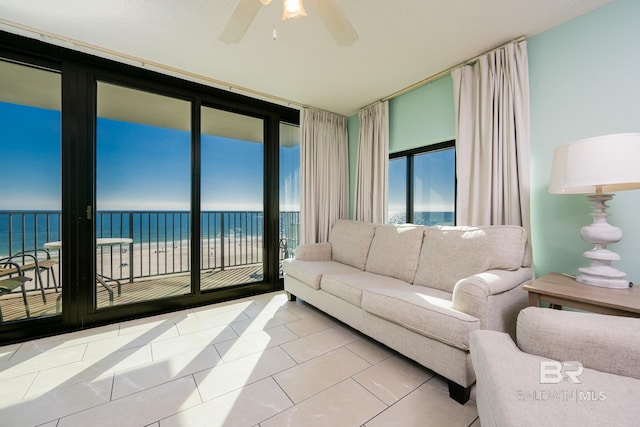 living room with a beach view, tile patterned flooring, ceiling fan, and a water view