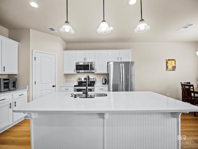 kitchen with a center island with sink, hanging light fixtures, and appliances with stainless steel finishes