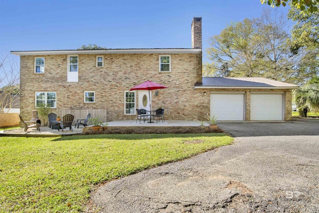 back of house with a chimney, brick siding, aphalt driveway, a lawn, and an attached garage