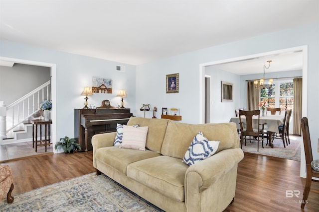 living room featuring an inviting chandelier, wood finished floors, visible vents, and stairs