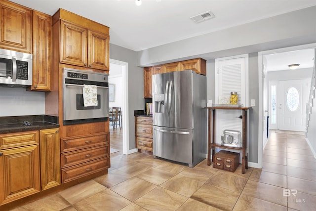 kitchen with dark stone countertops, visible vents, stainless steel appliances, baseboards, and brown cabinetry