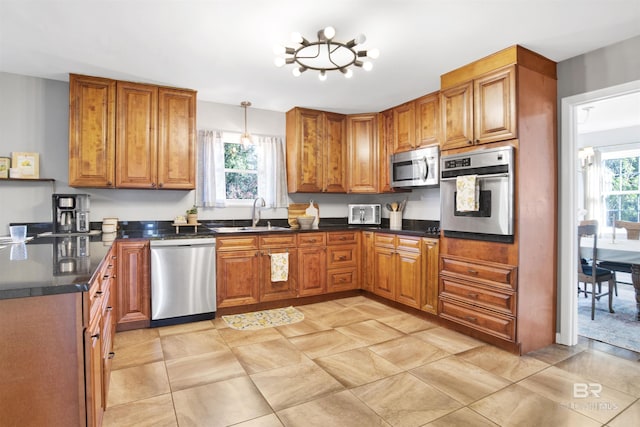 kitchen featuring appliances with stainless steel finishes, dark countertops, brown cabinetry, and a sink