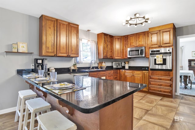 kitchen with a sink, brown cabinets, stainless steel appliances, a breakfast bar, and a peninsula