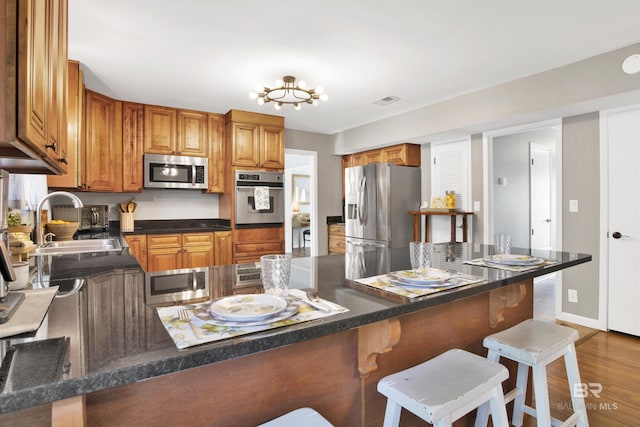 kitchen featuring a kitchen breakfast bar, brown cabinets, a sink, dark countertops, and stainless steel appliances