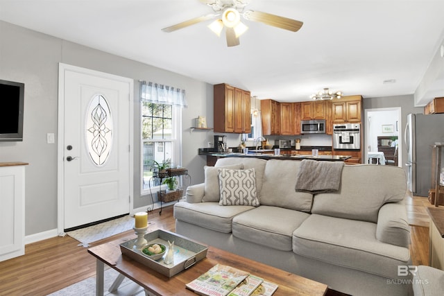 living room with baseboards, light wood-type flooring, and ceiling fan with notable chandelier