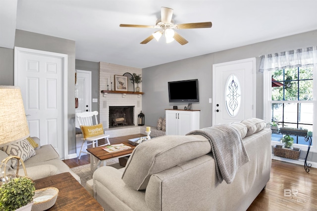 living room featuring wood finished floors, a ceiling fan, and a brick fireplace