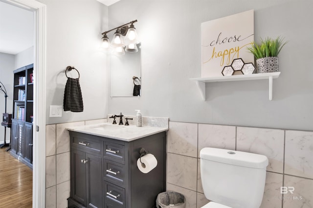 half bath featuring wood finished floors, tile walls, a wainscoted wall, toilet, and vanity