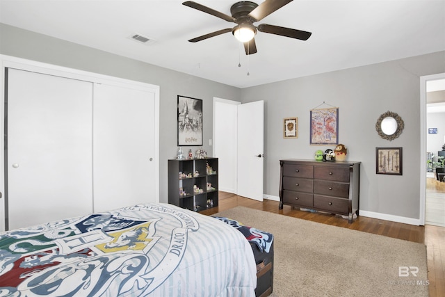 bedroom featuring wood finished floors, a closet, ceiling fan, baseboards, and visible vents