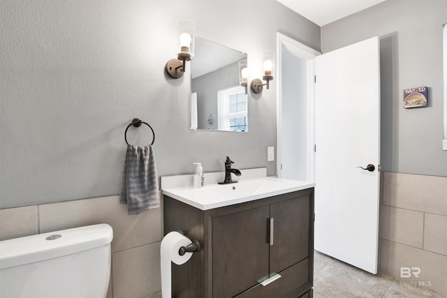 bathroom with toilet, tile walls, tile patterned flooring, and vanity
