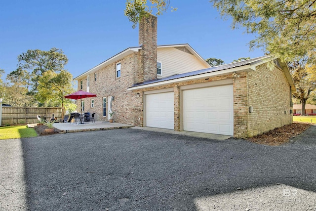 view of side of property featuring brick siding, aphalt driveway, a chimney, an attached garage, and fence