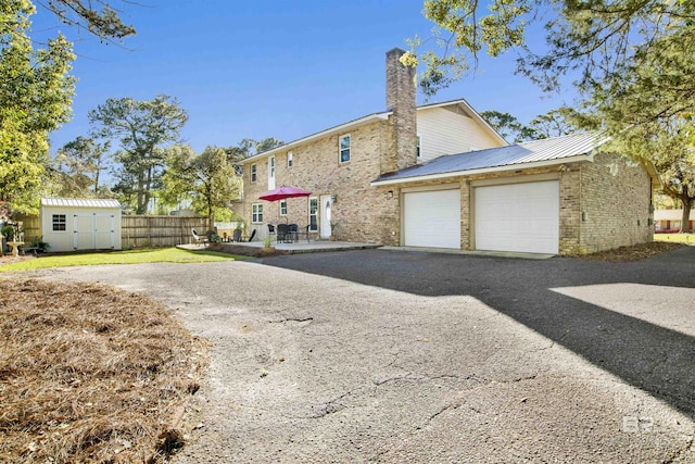 back of house featuring a garage, a chimney, aphalt driveway, brick siding, and a storage unit