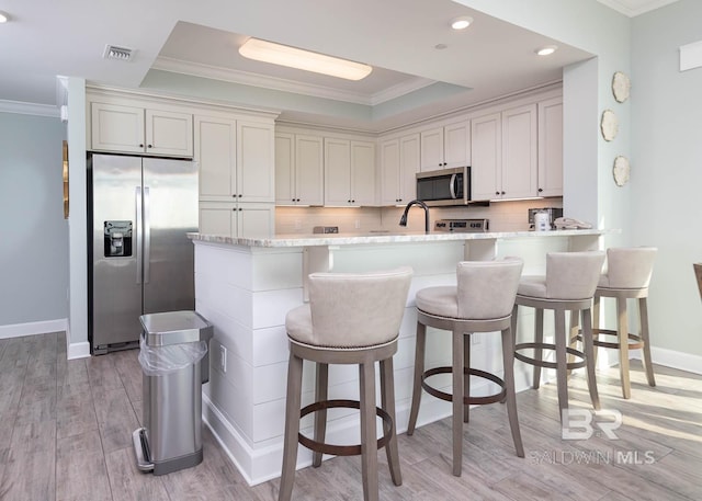 kitchen featuring backsplash, light wood-type flooring, appliances with stainless steel finishes, light stone counters, and a breakfast bar area