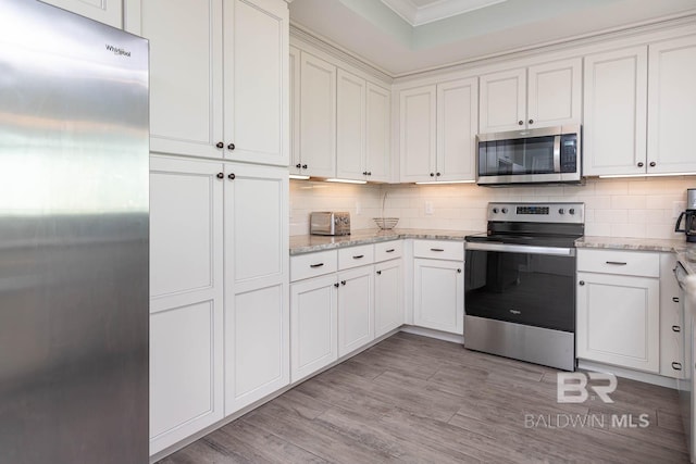 kitchen with white cabinets, backsplash, light wood-type flooring, light stone counters, and stainless steel appliances