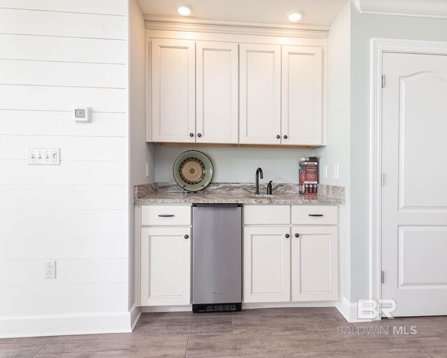 bar with white cabinetry, sink, light stone countertops, and light hardwood / wood-style floors