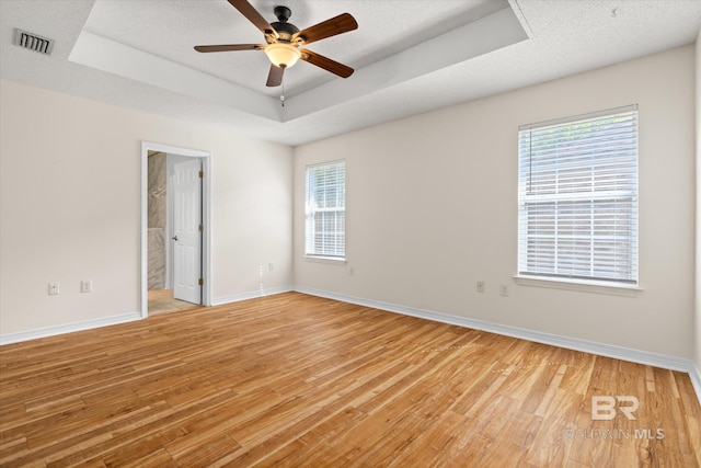 empty room with a wealth of natural light, a tray ceiling, visible vents, and light wood-style floors