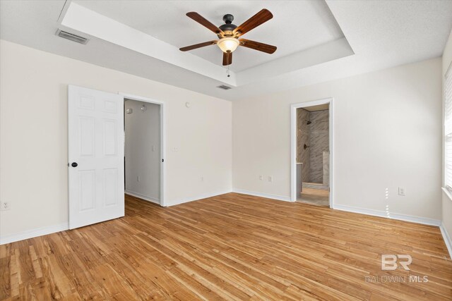 unfurnished bedroom with light wood finished floors, a tray ceiling, visible vents, and baseboards