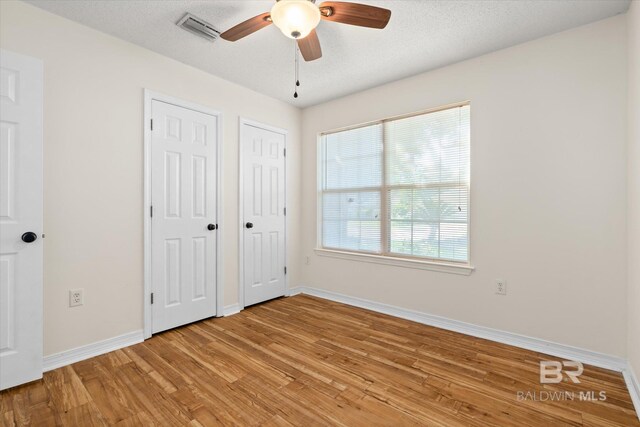 unfurnished bedroom featuring light wood finished floors, baseboards, visible vents, a textured ceiling, and multiple closets