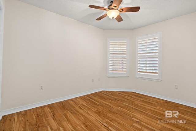 unfurnished room featuring a textured ceiling, wood finished floors, a ceiling fan, and baseboards