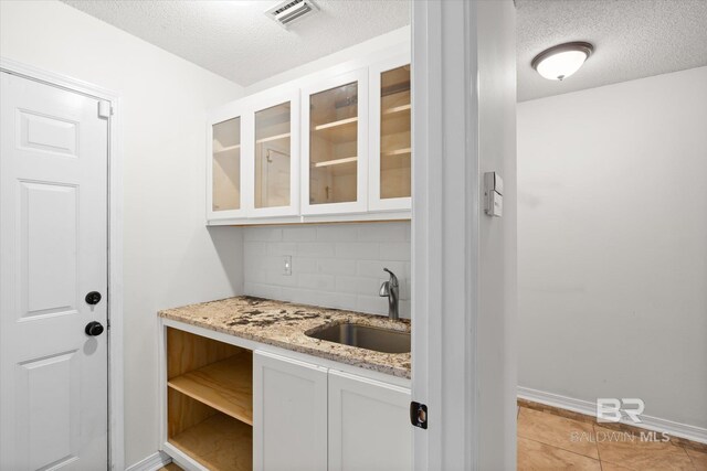 bar with light tile patterned floors, visible vents, backsplash, a sink, and a textured ceiling