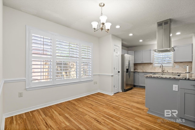 kitchen with gray cabinetry, light wood-style floors, stainless steel refrigerator with ice dispenser, tasteful backsplash, and island exhaust hood