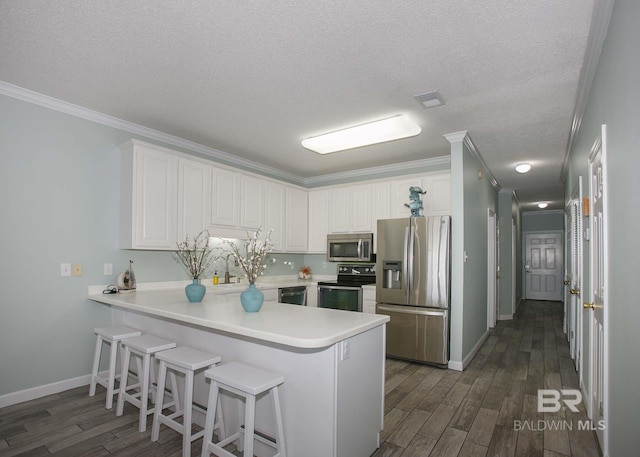 kitchen featuring dark hardwood / wood-style floors, kitchen peninsula, stainless steel appliances, and ornamental molding