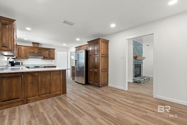 kitchen with under cabinet range hood, a peninsula, stainless steel appliances, and light wood-style flooring