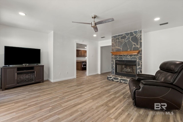 living room with visible vents, a stone fireplace, a ceiling fan, and wood finished floors