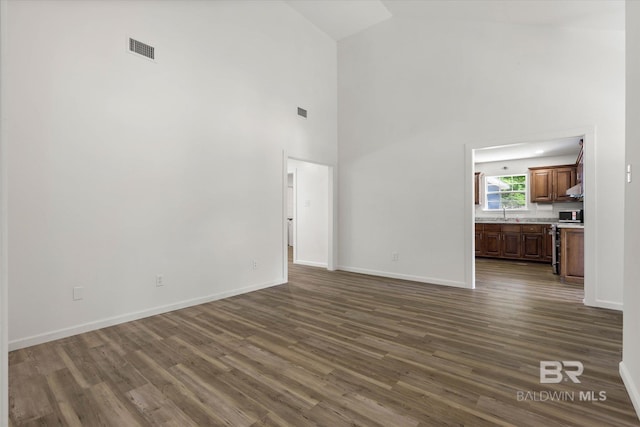 unfurnished living room with visible vents, baseboards, dark wood-type flooring, and high vaulted ceiling