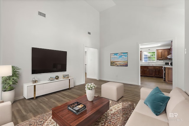 living area with baseboards, light wood finished floors, visible vents, and high vaulted ceiling