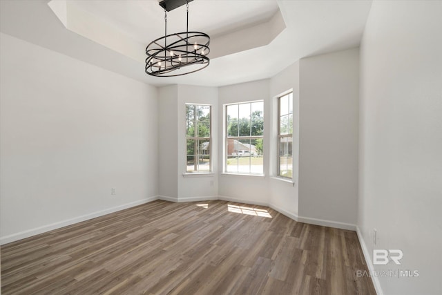 empty room with baseboards, a raised ceiling, a chandelier, and wood finished floors