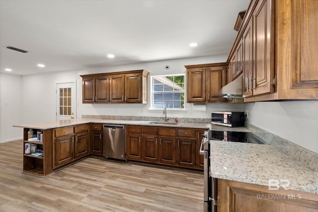 kitchen featuring under cabinet range hood, a sink, a peninsula, light wood-style floors, and stainless steel appliances