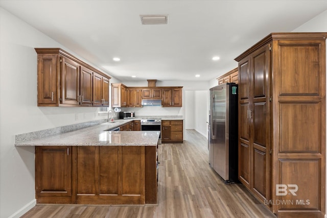 kitchen with a peninsula, a sink, light wood-type flooring, under cabinet range hood, and appliances with stainless steel finishes