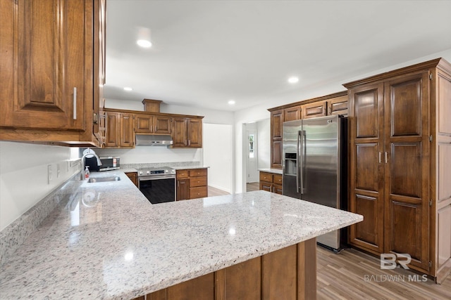 kitchen featuring a peninsula, a sink, under cabinet range hood, appliances with stainless steel finishes, and light stone counters