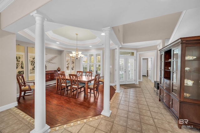 dining room featuring a tray ceiling, light tile patterned flooring, crown molding, baseboards, and ornate columns