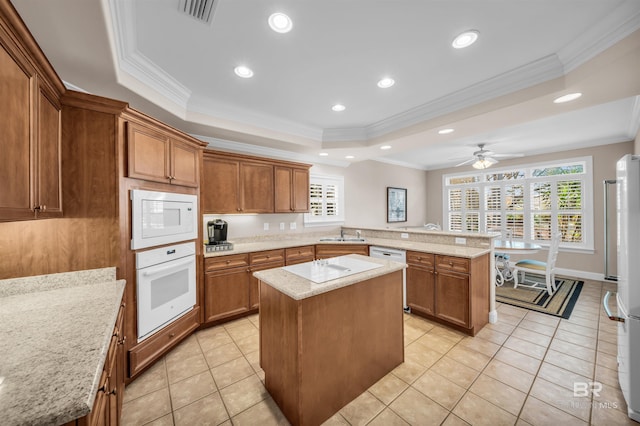 kitchen featuring a tray ceiling, a peninsula, brown cabinetry, white appliances, and visible vents