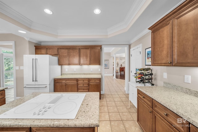 kitchen featuring a tray ceiling, brown cabinets, ornamental molding, and white appliances