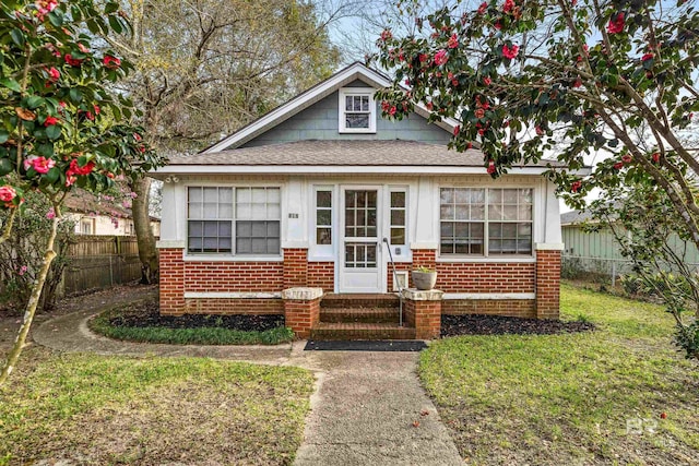 bungalow featuring entry steps, brick siding, roof with shingles, fence, and a front yard