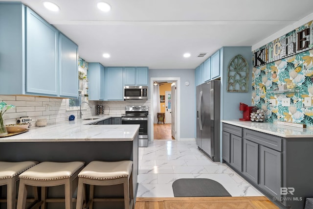 kitchen featuring stainless steel appliances, a breakfast bar, a peninsula, a sink, and marble finish floor