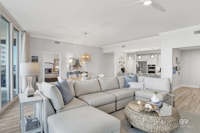 living area featuring visible vents, light wood-style flooring, ornamental molding, ceiling fan with notable chandelier, and baseboards