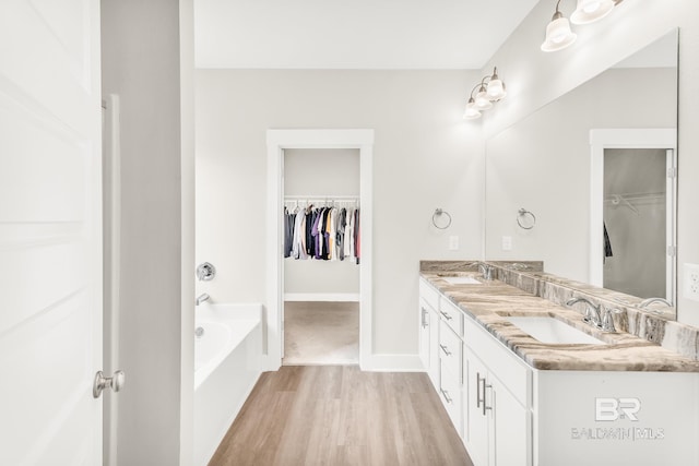 full bathroom featuring double vanity, wood finished floors, a sink, and a bath