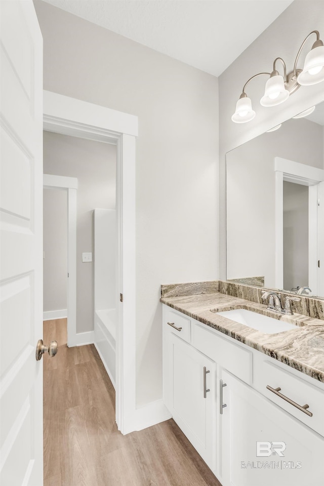 bathroom with a tub to relax in, vanity, baseboards, and wood finished floors