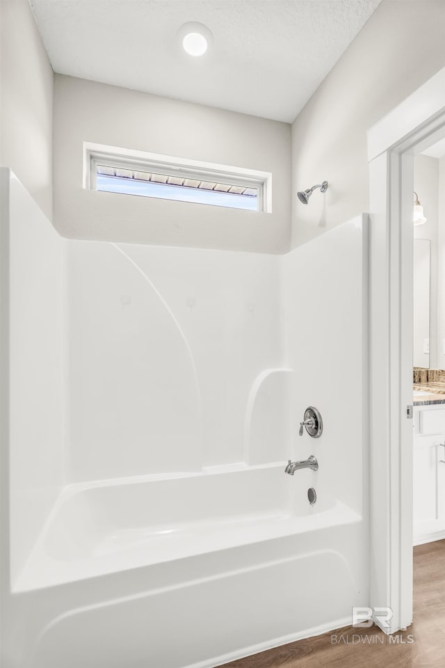 full bath featuring  shower combination, plenty of natural light, vanity, and wood finished floors