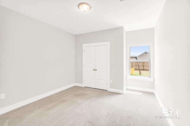 unfurnished bedroom featuring baseboards, a closet, and light colored carpet