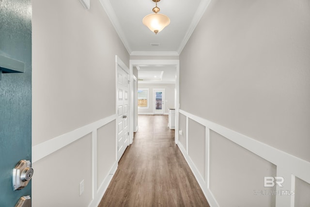 hallway featuring a wainscoted wall, ornamental molding, wood finished floors, and a decorative wall